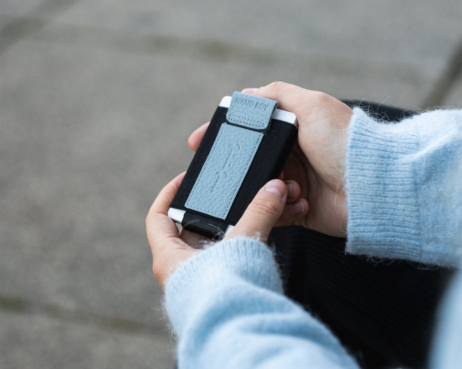 Nahaufnahme der Hände der Frau mit blauem Pullover. Sie hält den blauen Nano Boy Pocket und präsentiert seine Rückseite.