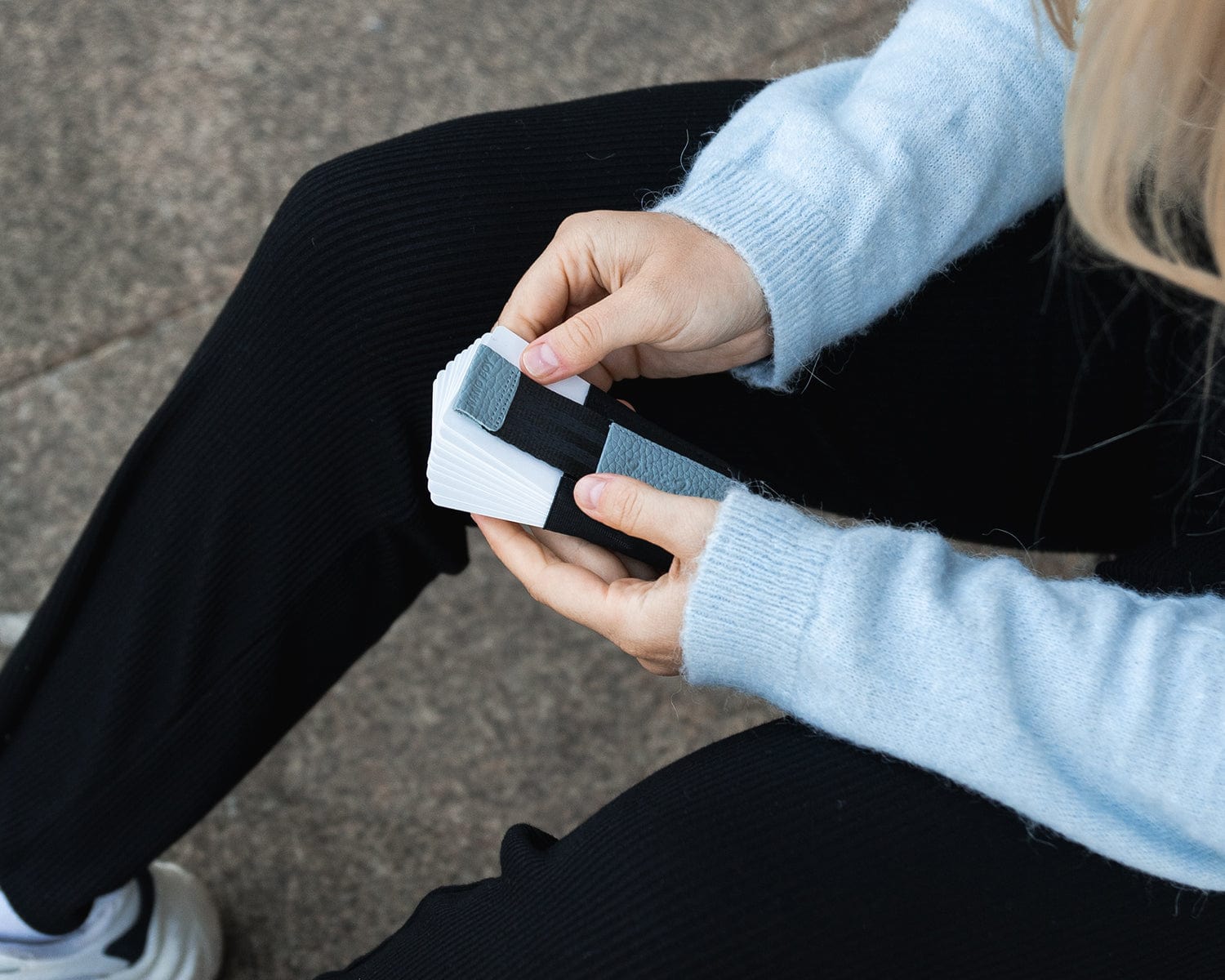 Blonde Frau mit blauem Pullover hält Nano Boy Pocket in der Farbe Blau in den Händen und zieht einige Karten heraus.