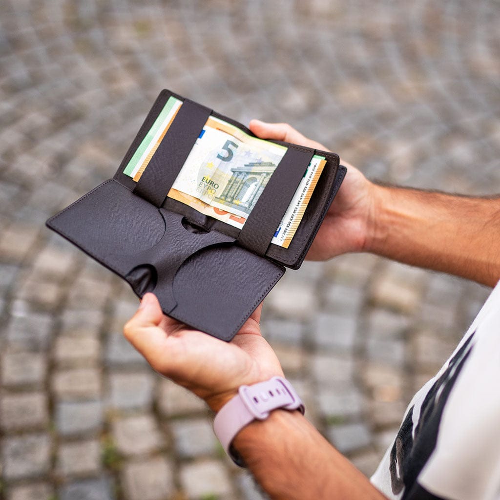 Person holding a black flapstar magic wallet wallet with money against a blurred cobblestone street background