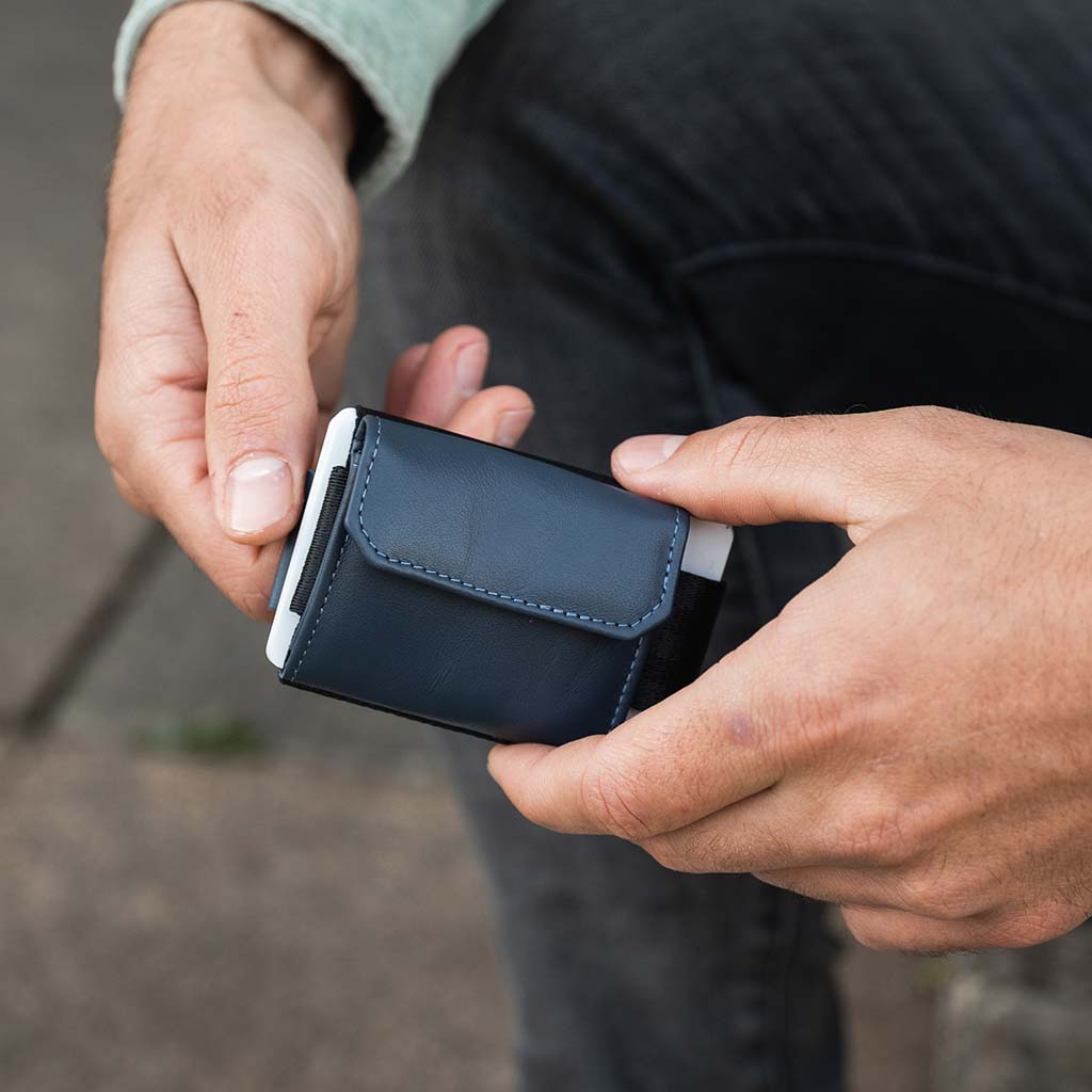 Person holding a small blue card holder with coin pocket from jaimie jacobs in front of  a blurred background