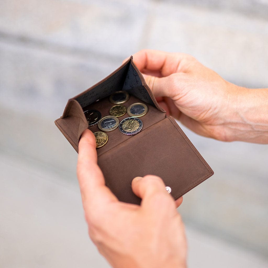 Brown leather slimstar wallet with coins held by a hand against a blurred background